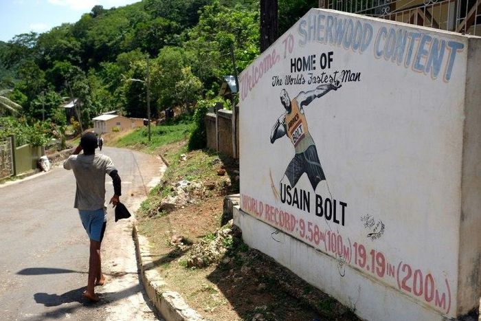 A boy walks past a welcome sign depicting Jamaican sprinter Usain Bolt at an intersection in his hometown of Sherwood Content, Jamaica
