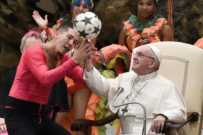 A Cuban circus artist helps Pope Francis juggle a football during his weekly audience on Wednesday
