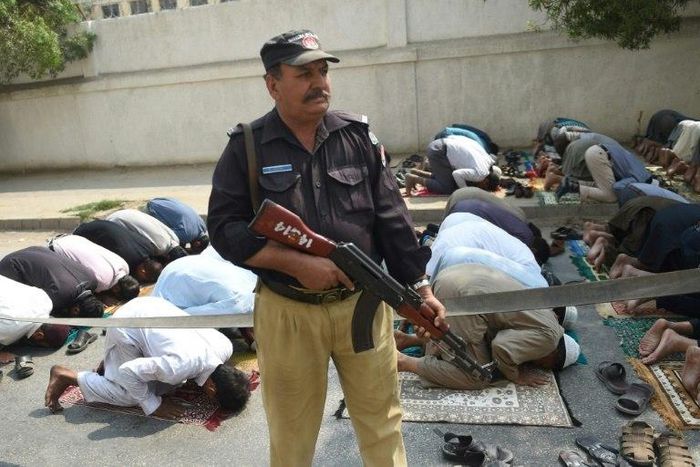 A Pakistani policeman stands guard as Muslims offer Friday prayers on a street in Karachi, on February 17, 2017