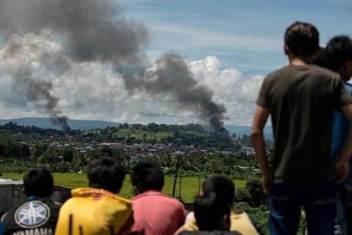People watch as smoke rises from houses after Philippine air force planes bombed Islamist militant positions in the city of Marawi on the southern island of Mindanao