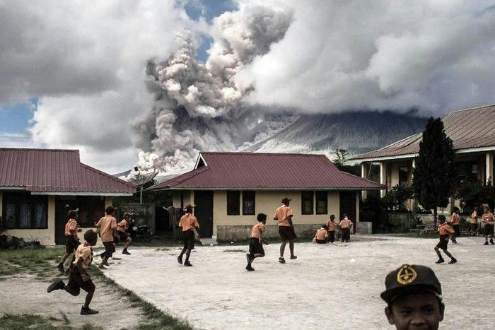 Children play at school as Indonesia's Mount Sinabung spews clouds of smoke and ash on February 10, 2017