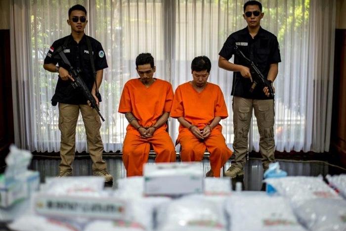 Indonesian narcotics police guard two suspects and the seized drugs during the press conference