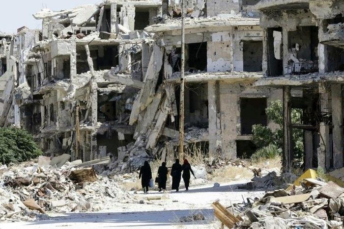 Women walk between destroyed buildings in the government-held Jouret al-Shiah neighbourhood of the central Syrian city of Homs