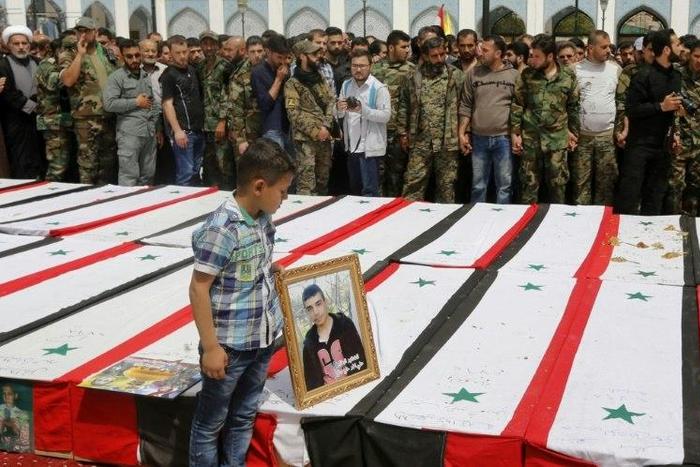 A Syrian boy places a picture on top of a coffin during a funeral ceremony at the Sayyida Zeinab shrine on the outskirts of Damascus on April 26, 2017 for victims of a bombing targeting evacuees from besieged government-held towns