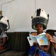 Women sitting under hair steamers read books from a mini-library at a hairdresser's in Abidjan.