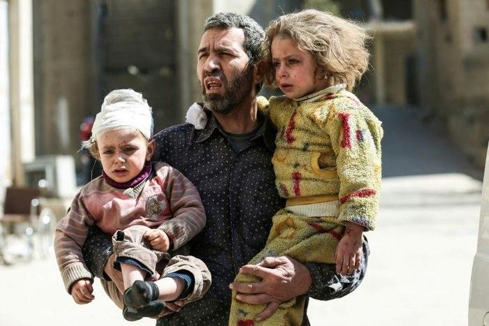 A Syrian man carries two injured children after a reported air strike in the rebel-controlled town of Hammuriyeh, on the outskirts of the capital Damascus, on March 25, 2017