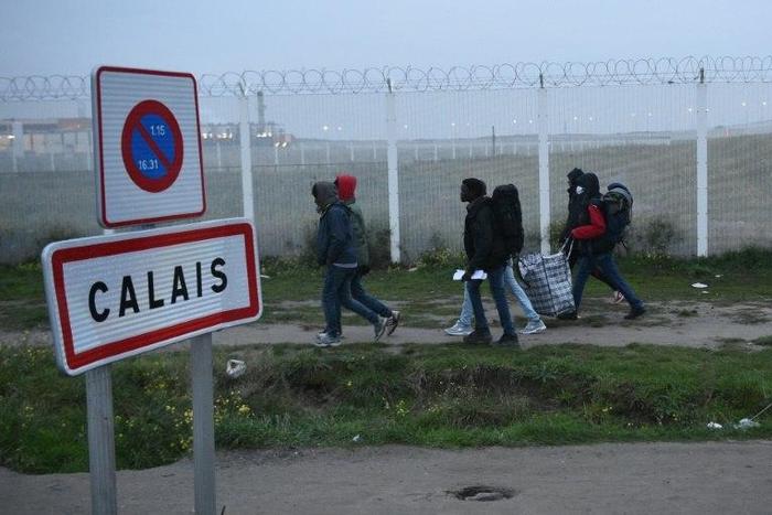 Migrants, carrying their luggage, walk past a Calais city limit sign as they head towards a meeting point set by French authorities as part of the full evacuation of the Calais "Jungle" camp, on October 24, 2016