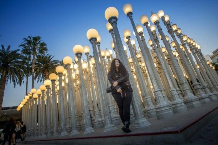 A young woman poses for a picture under "Urban Light" (2008), an assemblage of 202 antique street lamps by Chris Burden, one of LA's most photographed monuments