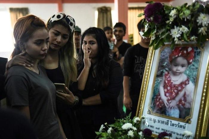 Jiranuch Trirat (L) is comforted by friends as she looks at a photograph of her 11-month-old daughter Natalie during funeral rites at a temple in Phuket, Thailand
