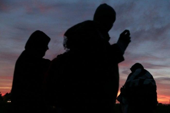 Migrants wait at dusk close to the "Jungle" migrant camp in Calais, northern France, on October 27, 2016, during a massive operation to clear the squalid settlement where 6,000-8,000 people have been living in dire conditions