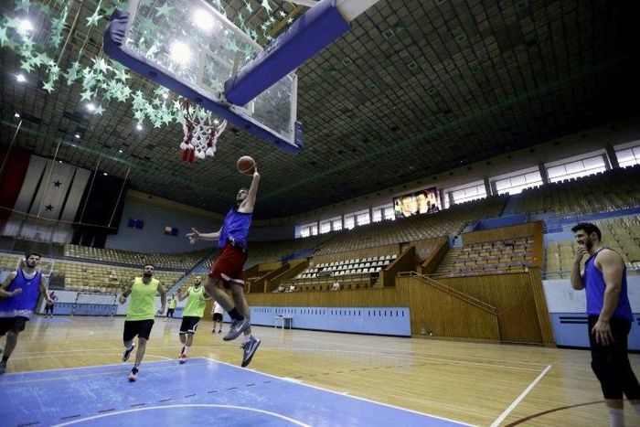 Syrian basketball team players take part in a training session at a stadium decorated with portraits of Syrian President Bashar al-Assad and his late father Hafez al-Assad (top R)