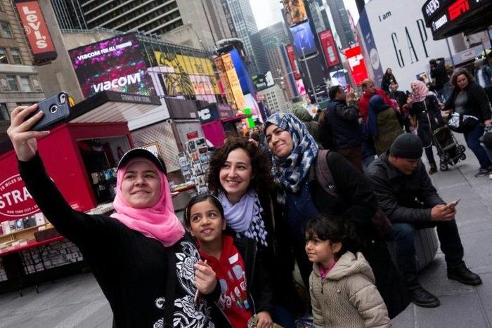 Syrian and Iraqi refugee families take selfies in Times Square during a tour of Manhattan in New York