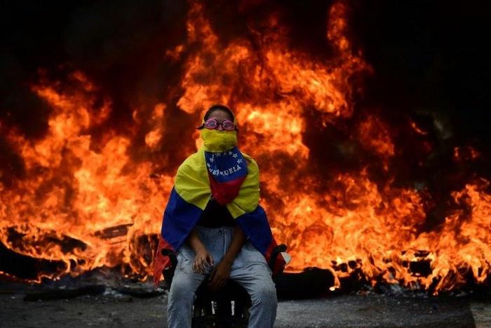 A Venezuelan opposition activist is backdropped by a burning barricade during a demonstration against President Nicolas Maduro in Caracas, on April 24, 2017