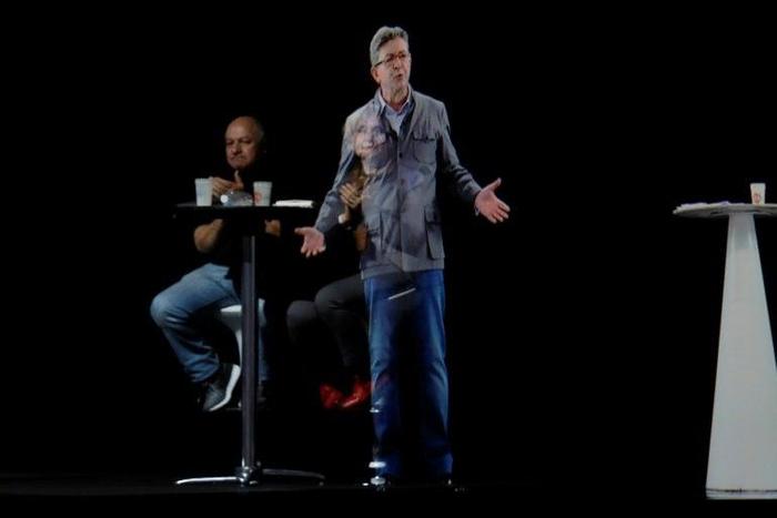 People sit near an hologram of French presidential election candidate Jean-Luc Melenchon (C) during a campaign meeting on February 5, 2017 in La Plaine Saint Denis, northern Paris