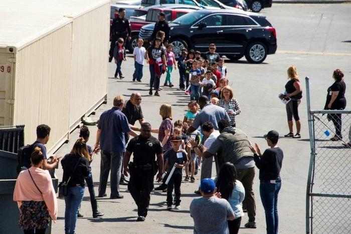 A police officer leads children to be reunited with parents after a gunman entered a classroom and killed one woman and one student, before turning the gun on himself, at North Park Elementary School in San Bernardino, California