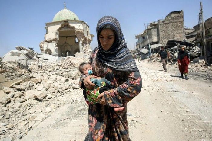 An Iraqi woman carrying a child walks by the destroyed Al-Nuri Mosque as she flees the Old City of Mosul on July 5, 2017
