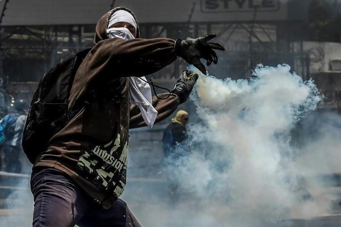 A demonstrator protesting against President Nicolas Maduro's government throws back a tear gas grenade at riot police, in Caracas, on April 10, 2017