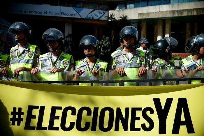 Riot police stand behind a banner that reads "Elections now" in fornt the National Electoral Council (CNE) in Caracas on January 2, 2017