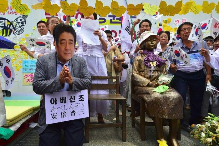 A man (L) wearing a mask of Japanese Prime Minister Shinzo Abe kneels down in a mock apology next to the statue (R) of a teenage girl symbolizing former "comfort women" who served as sex slaves for Japanese soldiers during World War II