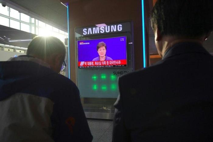 People watch a television news report showing South Korean President Park Geun-Hye making a public apology, at a railway station in Seoul.