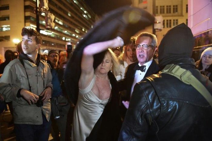 A woman throws her fur coat over her head outside the National Press Club in Washington, DC on January 19, 2017 as protesters shouted at them as they left the "Deploraball" event in honour of new US president Donald Trump
