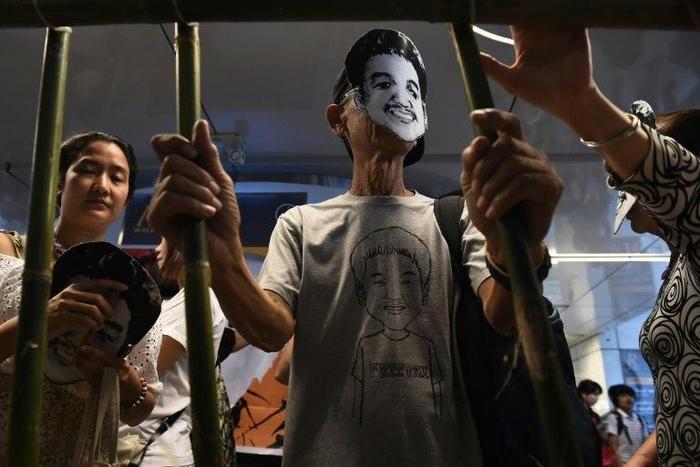 Activists standing behind makeshift bars wearing masks of Thai human rights activist Jatupat “Pai” Boonpattararaksa, who was arrested in early December 2016