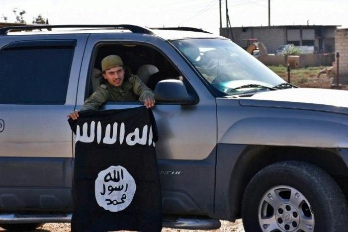 A member of the Syrian pro-government forces holds an Islamic State (IS) group flag after they entered the village of Dibsiafnan on the western outskirts of the Islamist's Syrian bastion of Raqa on June 11, 2017