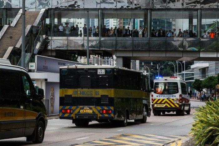 Bystanders watch as a prison van (C) transporting British banker Rurik Jutting, accused of the murders of two Indonesian women, leaves the High Court escorted by a police convoy in Hong Kong in the city's biggest murder case for years