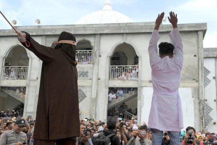 A religious officer canes an Acehnese man (R) for spending time in close proximity with a woman who is not his wife, which is against Sharia law, in Banda Aceh