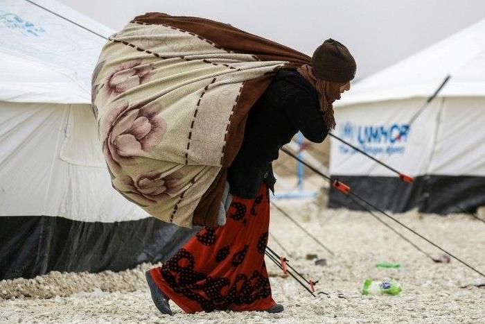 A displaced Syrian woman fleeing from Deir Ezzor, a city besieged by IS group fighters, carries blankets through a refugee camp in al-Hol, near the Iraqi border in northeastern Syria's Hasakeh province, on February 1, 2017