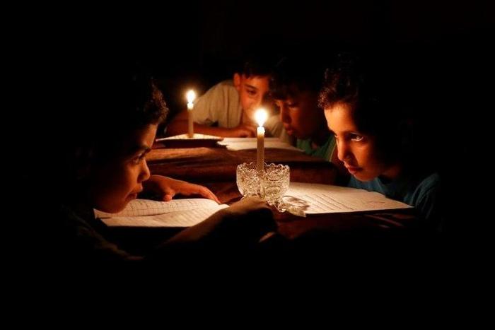 A picture taken on June 13, 2017 shows Palestinian children at home reading books by candle light due to electricity shortages in Gaza City