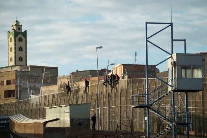 African immigrants sit on a border fence separating Morocco from the Spanish enclave of Melilla in 2014
