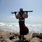 An armed Somali pirate walks along the coastline near Hobyo in 2010