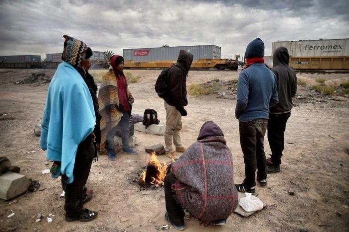 Migrants warm themselves next to a campfire near train tracks in Sonora state, Mexico close to the border with the United States