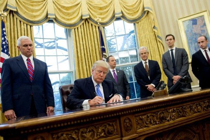 US President Donald Trump signs an executive order alongside officials including National Trade Council Advisor Peter Navarro (3rd R) in the Oval Office of the White House in Washington, DC, on January 23, 2017