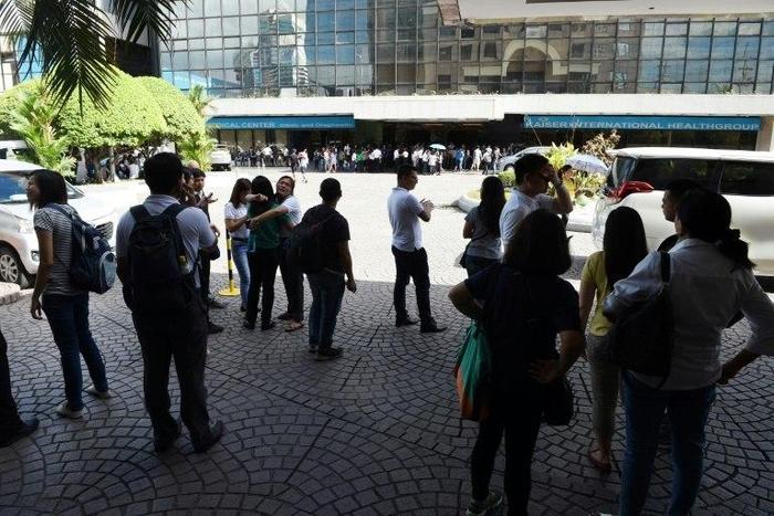 Office workers stand on the grounds of an office building in the financial district of Makati in Manila on April 8, 2017, after a 5.7 magnitude earthquake struck