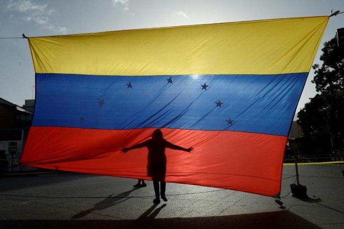 A protester's shadow is cast on a Venezuelan national flag in Caracas, the capital city of a country that has hit its 100th day of anti-government protests