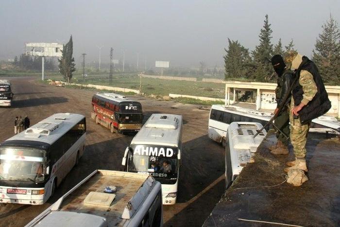 Syrian opposition fighters stand on top of a vehicle in rebel-held Rashidin, west of Aleppo city, as buses carrying people from government-held Fuaa and Kafraya arrive as part of an evacuation deal