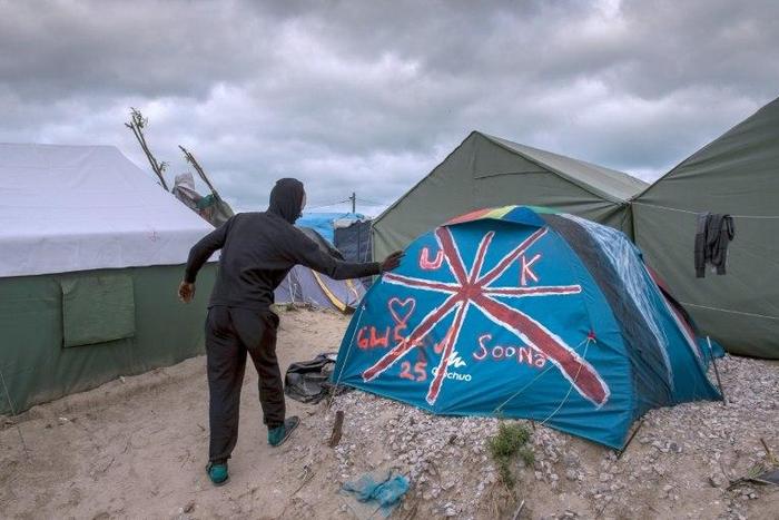 A Sudanese man stands next to a tent painted with the British flag at the "Jungle" migrant camp in Calais on October 12, 2016