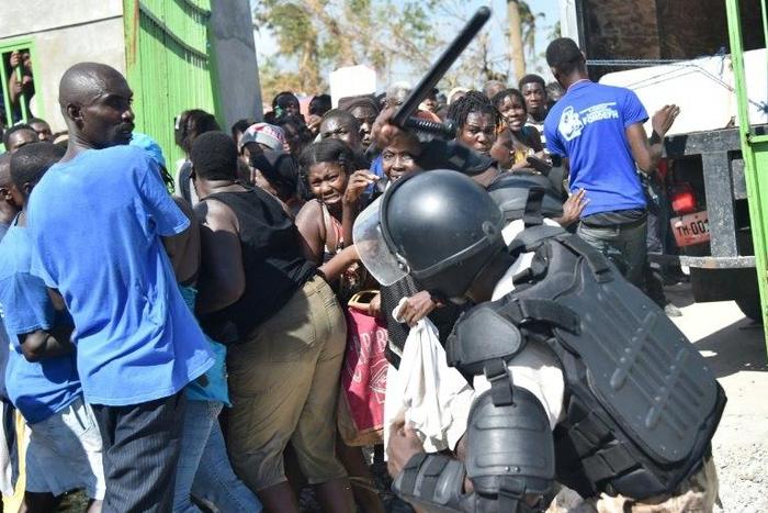 A Haitian policeman pushes back Hurricane Matthew victims waiting for the delivery of food from the UN's World Food Programme in Tobeck, in Les Cayes