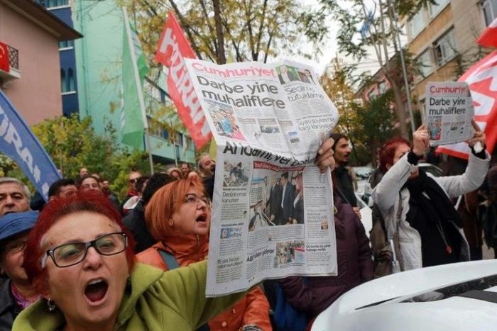 People hold the latest copy of Turkish newspaper Cumhuriyet outside its headquarters in Ankara, chanting that a free media could not be silenced