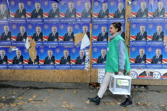 An official carries a ballot box past election posters during the parliamentary polls in Tbilisi on October 30, 2016
