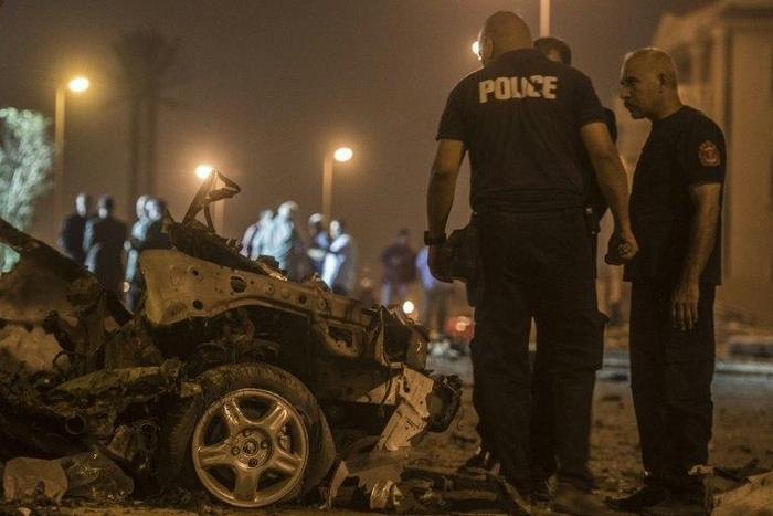 Egyptian policemen inspect the wreckage of a car bomb that exploded in a Cairo suburb after Egypt's deputy prosecutor general drove by wounding a passerby