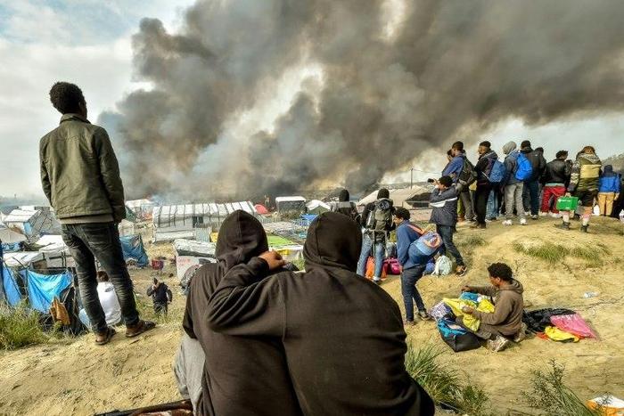 Migrants looks at the smoke rising from fires in the "Jungle" migrant camp in Calais on October 26, 2016