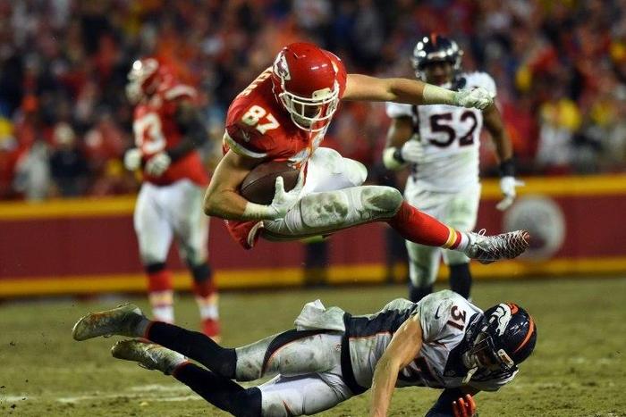Tight end Travis Kelce of the Kansas City Chiefs leaps over free safety Justin Simmons of the Denver Broncos during their game at Arrowhead Stadium in Kansas City, Missouri, on December 25, 2016