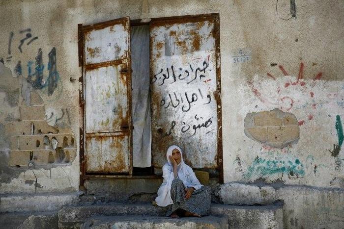 An elderly Palestinian woman sits in front of her house in Gaza City