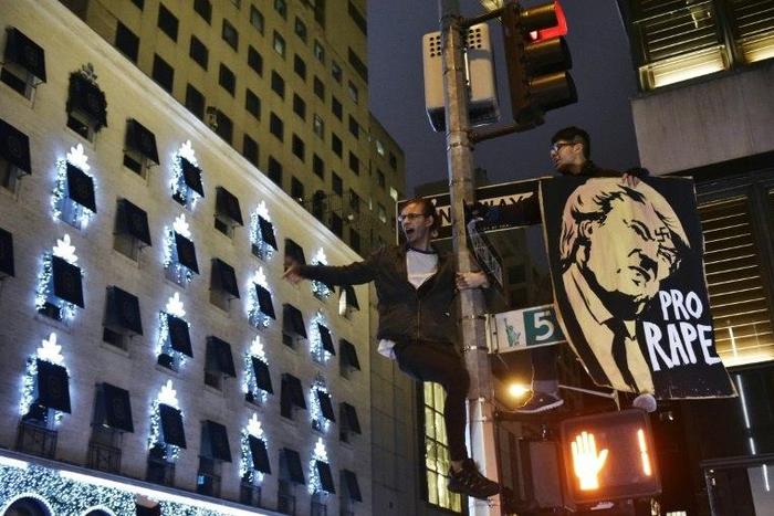 Protestors shout slogans from a lampost during a demonstration across from Trump Tower in New York