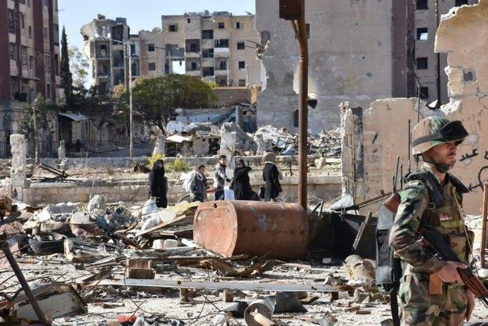 Syrians walk amid debris as a soldier secures the Masaken Hanano neighbourhood in Aleppo, on December 6, 2016