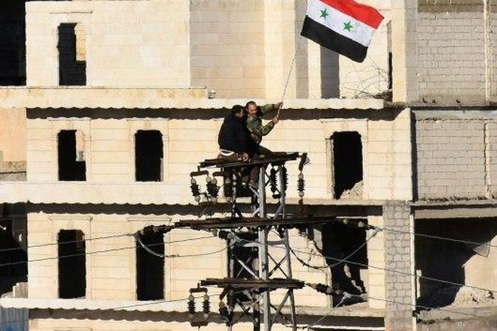 Syrian pro-government forces wave the Syrian flag on top of an electricity pole as buses evacuate rebel fighters and their families from rebel-held neighbourhoods in Aleppo
