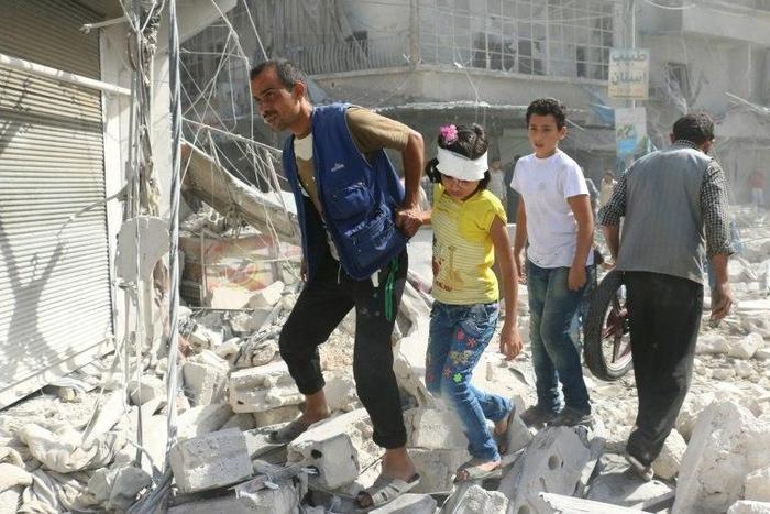 Syrians walk over rubble following air strikes on Aleppo on October 12, 2016